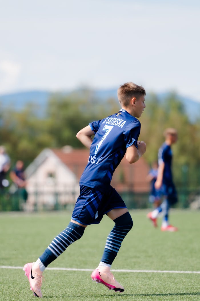 Boy in blue soccer uniform running during a game on a clear day.
