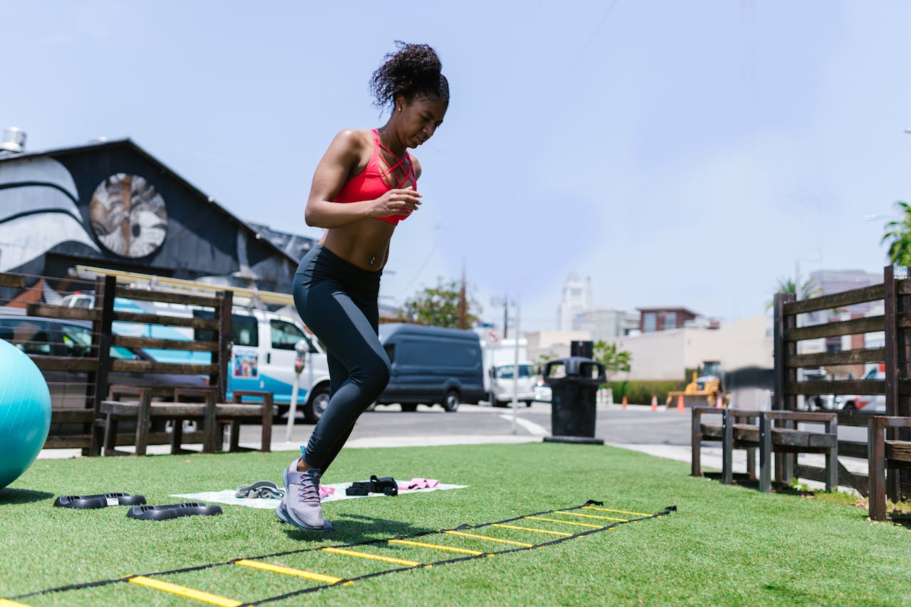Black woman performing fitness exercises using agility ladder outdoors